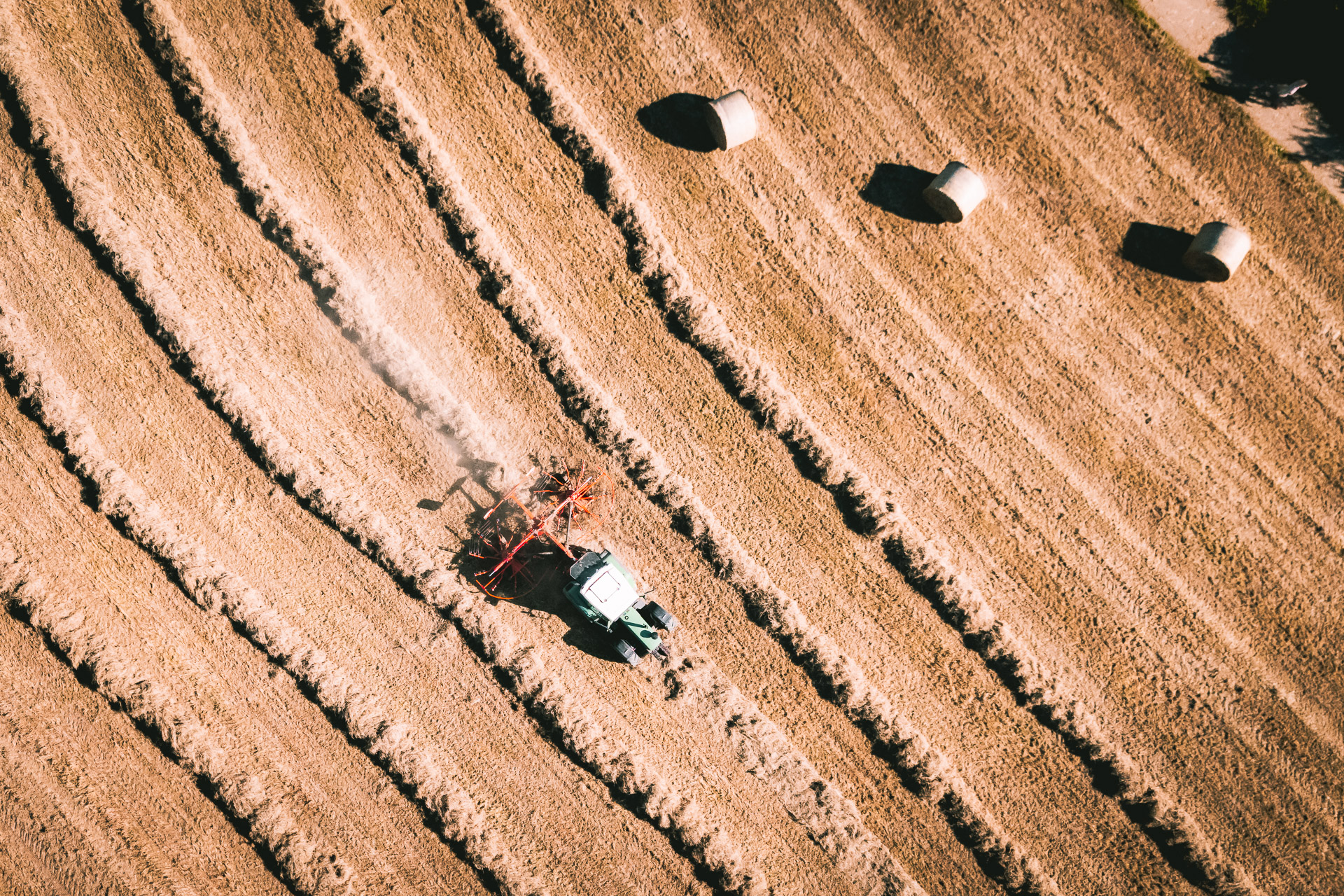 Drohnenaufnahme eines Traktors beim Heuwenden auf dem Feld.