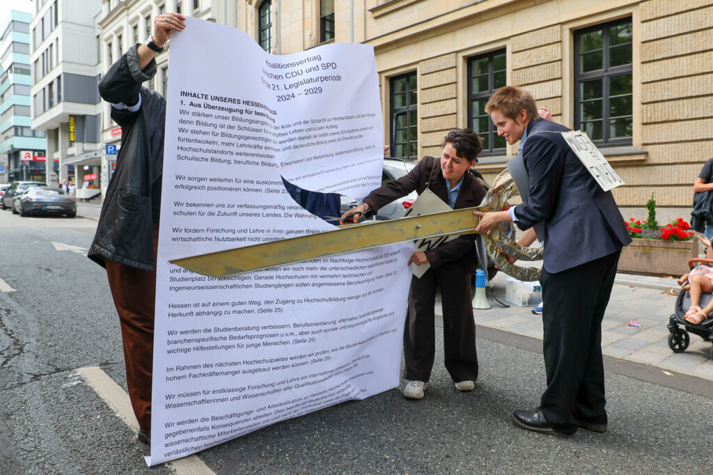 Zwei Teilnehmerinnen der Kundgebung gegen Hochschul-Kürzungen zerschneiden symbolisch den Koalitionsvertrag zwischen CDU und SPD vor dem Hessischen Ministerium für Wissenschaft und Forschung, Kunst und Kultur.