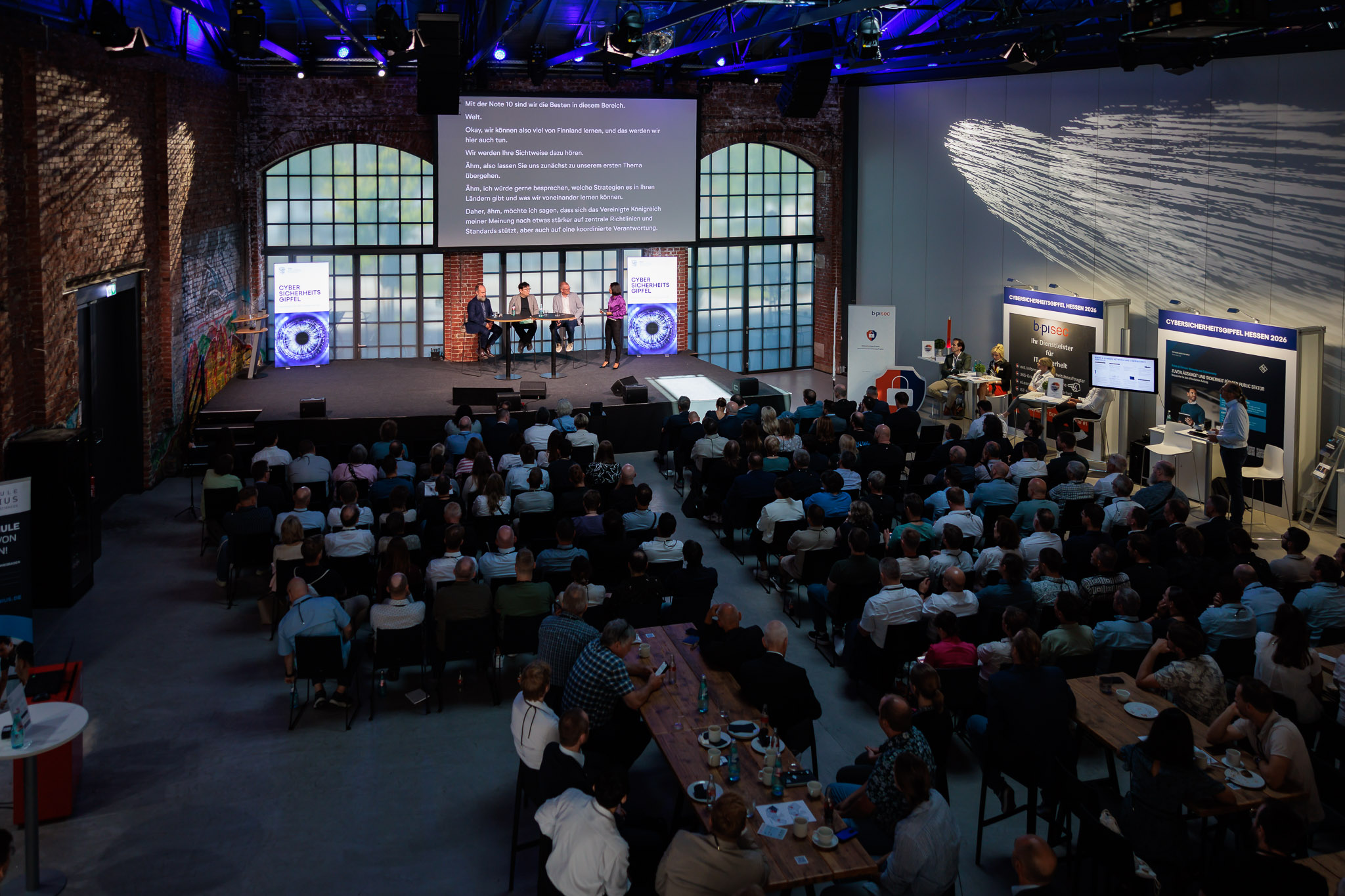 Fotografische Begleitung einer Konferenz mit zahlreichen Gästen, Podiumsdiskussion und Präsentationen auf der Bühne in einer modernen Veranstaltungslocation mit industriellem Charakter.