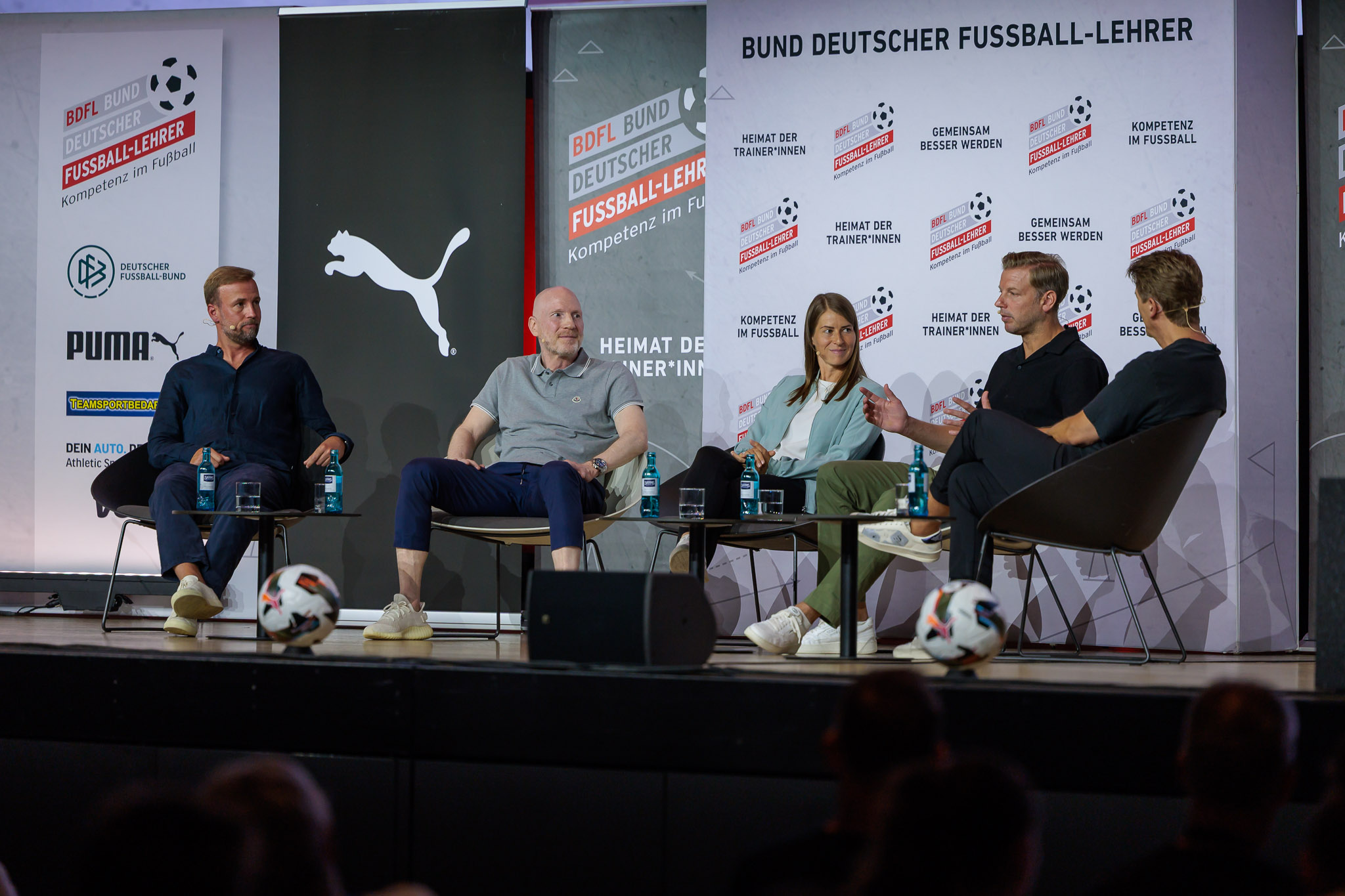 Podiumsdiskussion mit vier Teilnehmern beim Bund Deutscher Fußball-Lehrer (BDFL). Experten diskutieren auf der Bühne über aktuelle Themen im Fußball und Trainerwesen.
